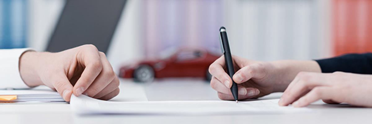 Renting de Automoción y Equipamientos - Manos firmando un contrato en una oficina con un coche de fondo