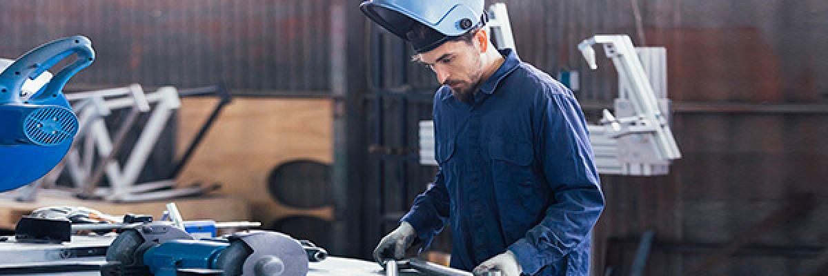  Seguro Multirriesgo Industrial - Hombre con casco y mono azul soldando metal en un taller